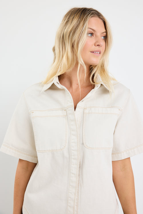 model wears an ecru denim short sleeve shirt with black pants
