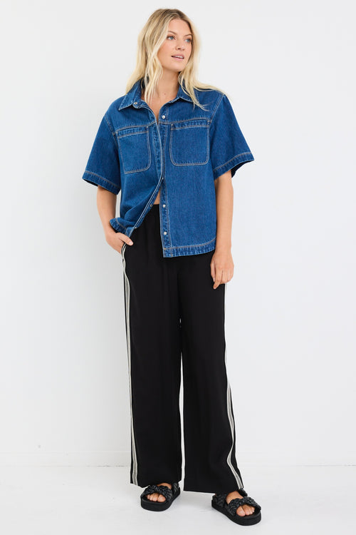 model wears a blue short sleeve denim shirt with black pants