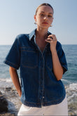 Woman wearing a denim shirt standing on a beach with ocean in the background