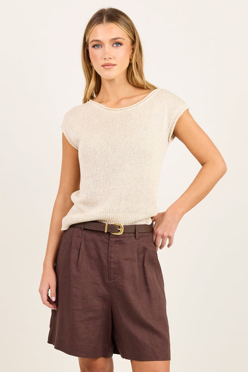 A woman modeling a cream short-sleeve knit top and dark brown linen shorts with a gold belt, standing against a plain off-white studio background.