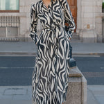 Woman in a zebra print dress standing on a street corner with a building in the background