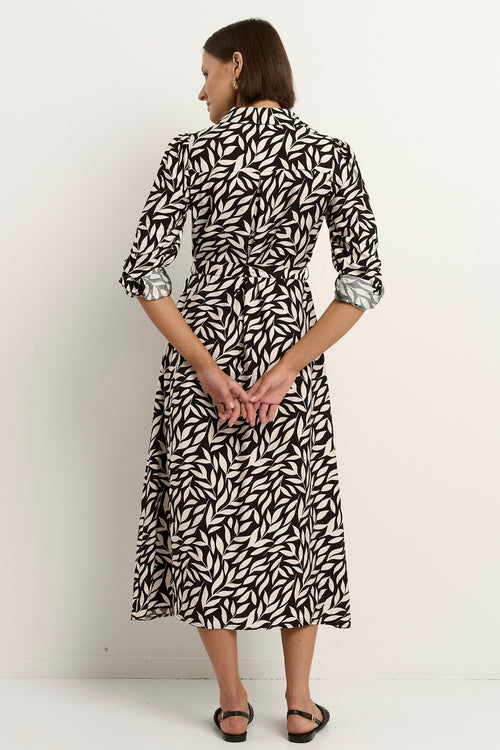 Woman wearing a black-and-white leaf-print midi dress with a relaxed button-down design and long sleeves, styled with black woven flats.







