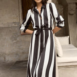 Woman wearing a black and white vertically striped midi dress with long sleeves and tie waist.