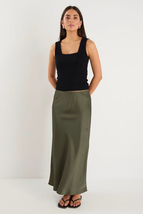 the model wears a khaki green maxi skirt with a black tank top