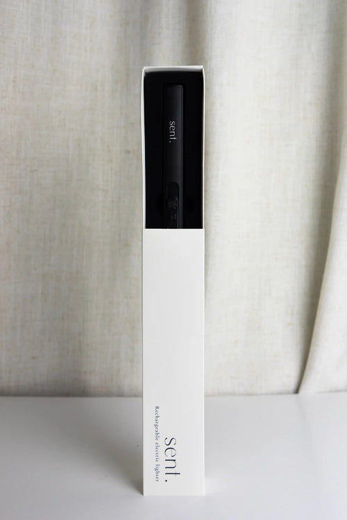 A tall, narrow white product box standing upright on a white surface, with a black vape device partially visible inside near the top. The box is branded 'sent.