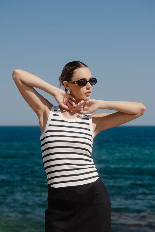 Woman in a striped tank top and sunglasses by the ocean