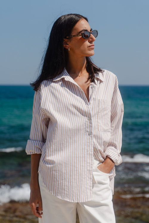 Woman in a striped shirt and sunglasses standing on a beach with ocean in the background