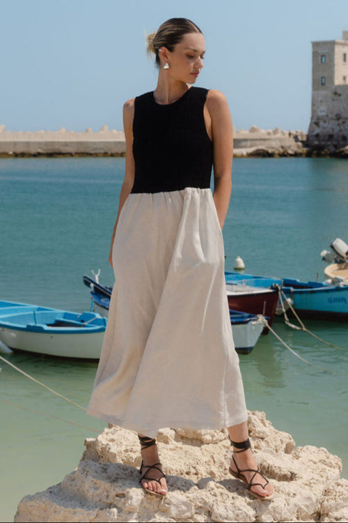 Woman standing on rocks by a harbor with boats and a clear sky