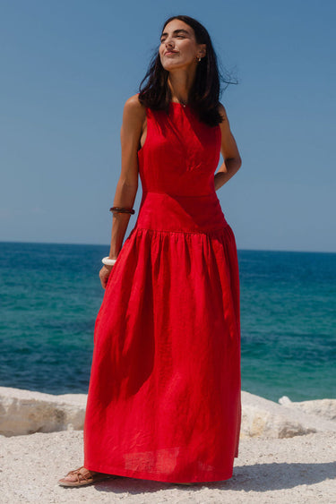 Woman in a red dress standing by the ocean on a clear day