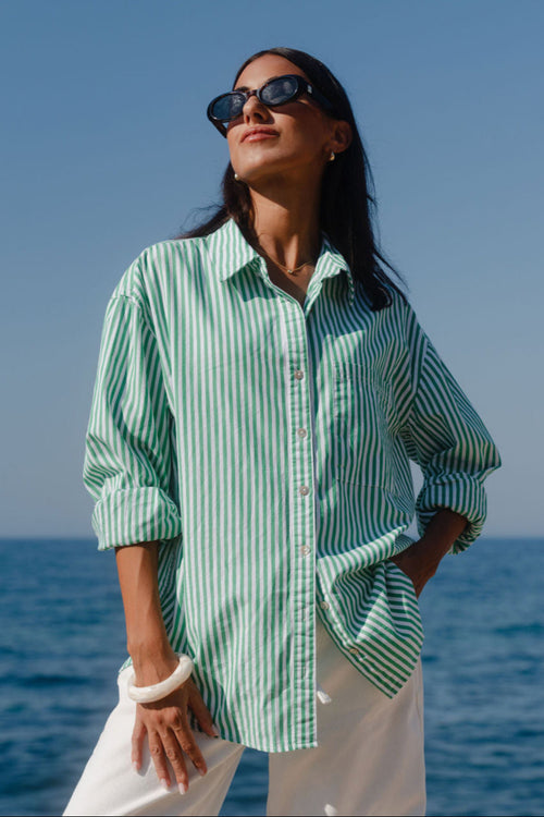 Woman wearing a green and white striped shirt and sunglasses by the ocean.