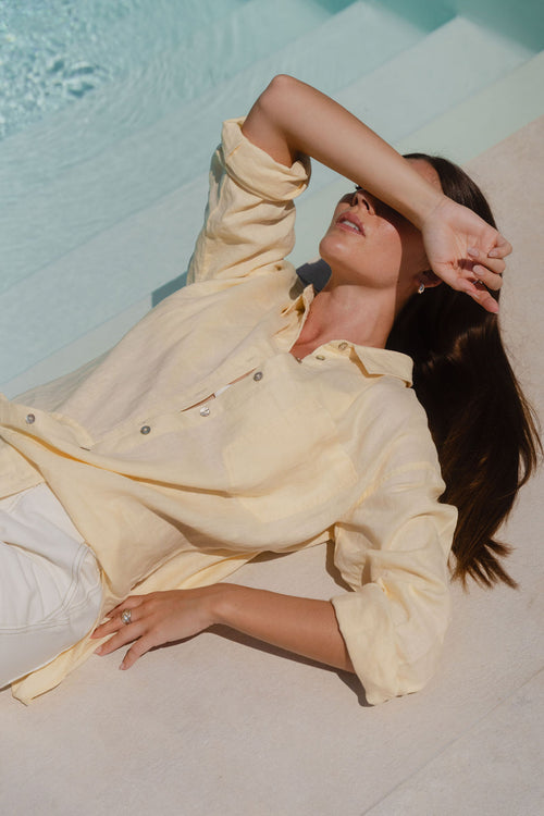 Woman in a light yellow outfit lying on a towel by a pool