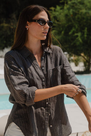 Woman standing by a poolside wearing sunglasses and a striped shirt.