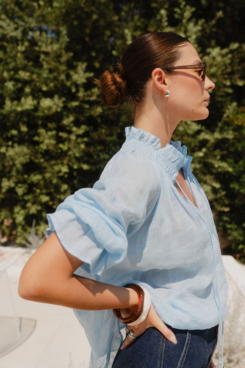 Woman wearing a light blue blouse with ruffled sleeves against a green outdoor background