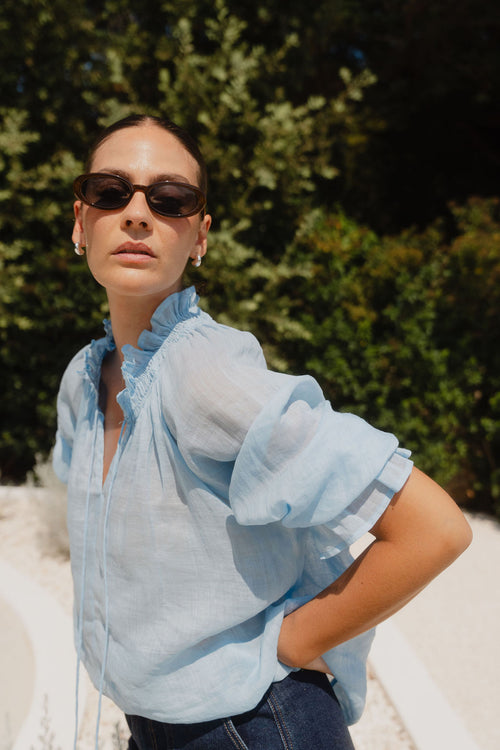 Woman wearing a light blue blouse with ruffled sleeves against a blurred green background