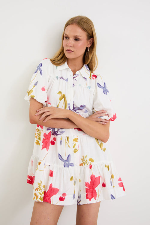 Model wearing a cream mini tiered shirt dress with colourful poppy floral print, puff sleeves and a button front.