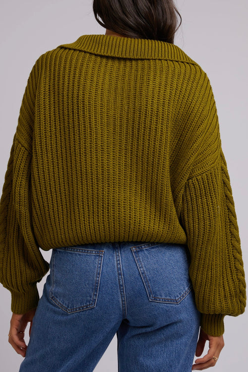 Model wears green knit and blue jeans