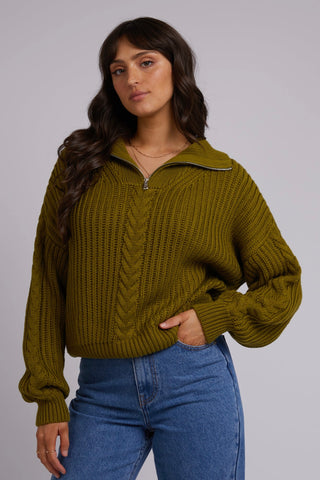 Model wears green knit and blue jeans