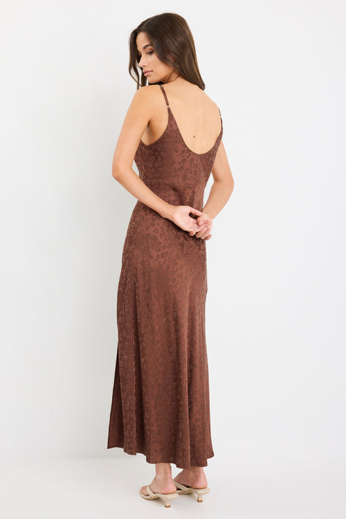 Woman wearing a chocolate brown strappy bias-cut midi dress with a subtle animal print and front slit, styled with cream heeled sandals.