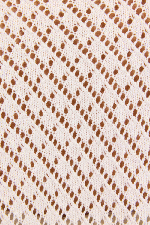 Close-up of a cream-colored knit fabric with a repeating diagonal lattice pattern of small openwork diamond shapes.