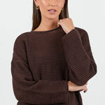 Woman wearing a brown textured sweater and blue jeans on a white background