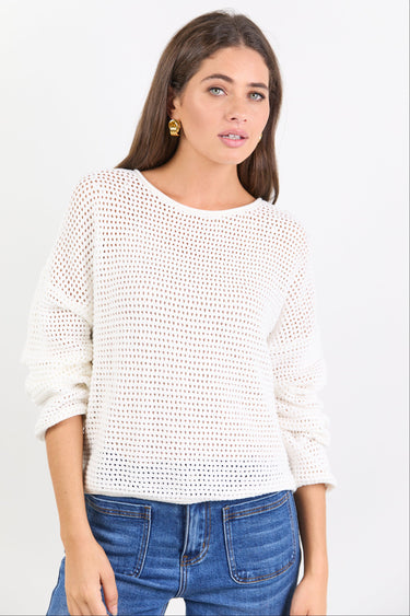Woman wearing a white textured sweater and blue jeans on a light gray background