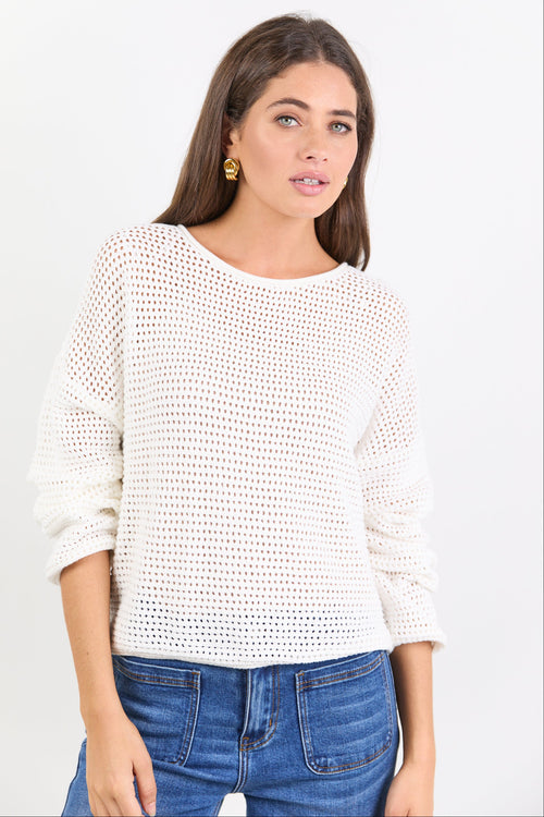 Woman wearing a white textured sweater and blue jeans on a light gray background
