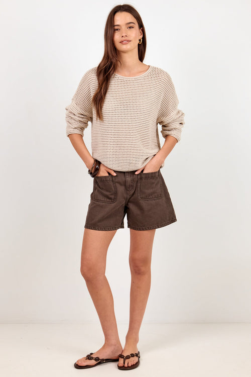 A woman modeling a beige textured knit long-sleeve top and dark brown shorts against a plain white studio background.