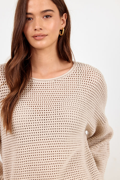 A woman wearing a beige open-knit crewneck sweater, shown from the chest up against a plain white background.