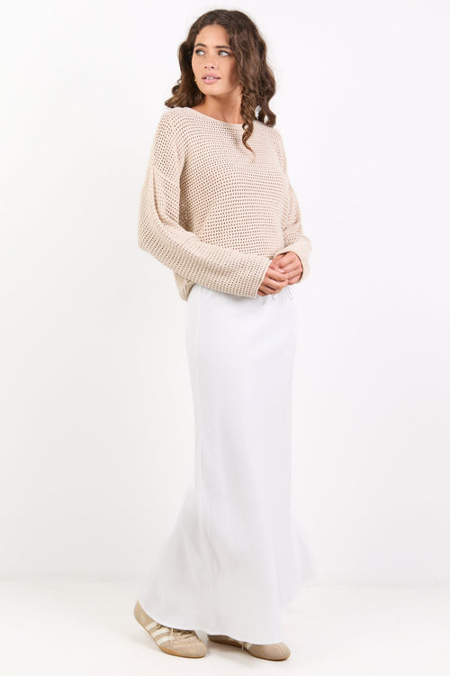 Woman wearing a beige sweater and white skirt on a white background