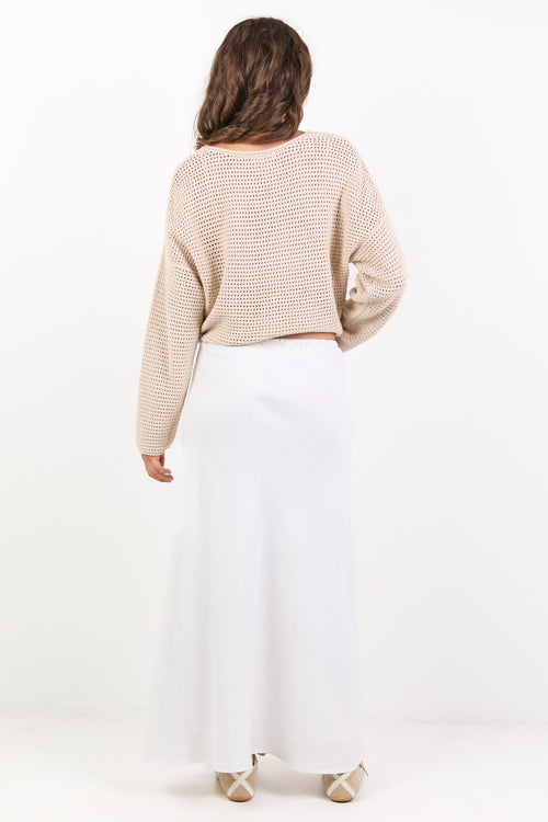 Person wearing a beige sweater and white skirt on a white background