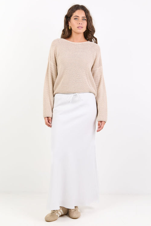 Woman wearing a beige sweater and white pants on a white background
