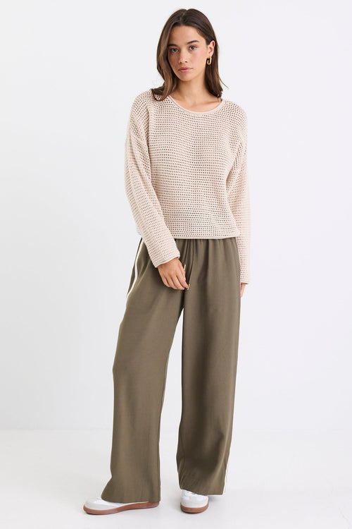 Woman wearing a beige sweater and olive green pants on a white background