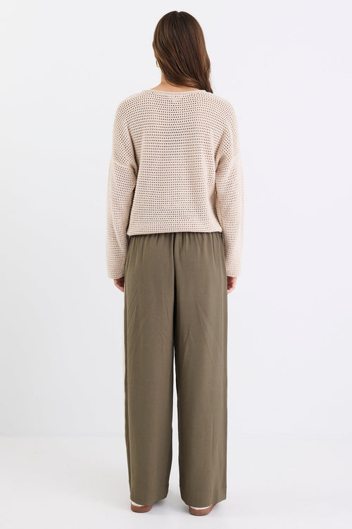 Woman wearing a beige sweater and olive green pants on a white background