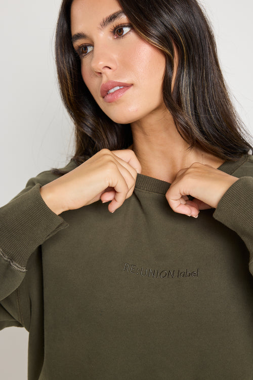 Model wears a khaki green long sleeve sweatshirt 