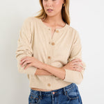Woman wearing a beige cardigan and blue jeans against a white background