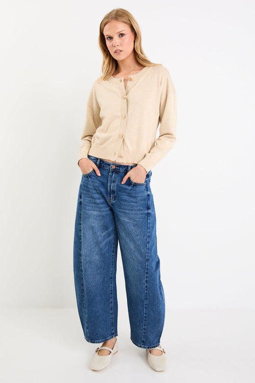Woman wearing a beige cardigan and blue jeans on a white background
