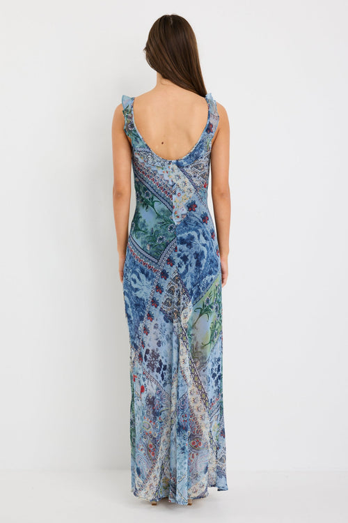 Woman wearing a blue maxi dress with a paisley scarf print, ruffle shoulder straps, and flowing bias-cut silhouette.