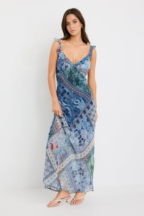 Woman wearing a blue maxi dress with a paisley scarf print, ruffle shoulder straps, and flowing bias-cut silhouette.