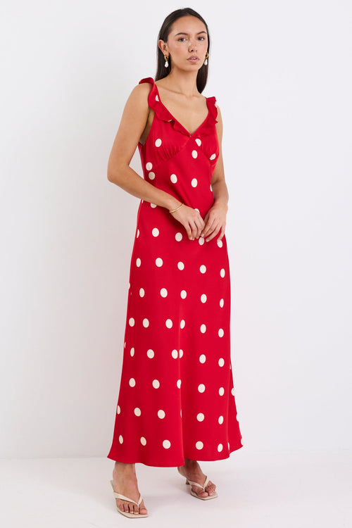 Woman wearing a red satin maxi dress with white polka dots, strappy sleeves, and a flattering bias-cut design.