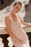 Woman in a white dress with red polka dots sitting on a stone bench.