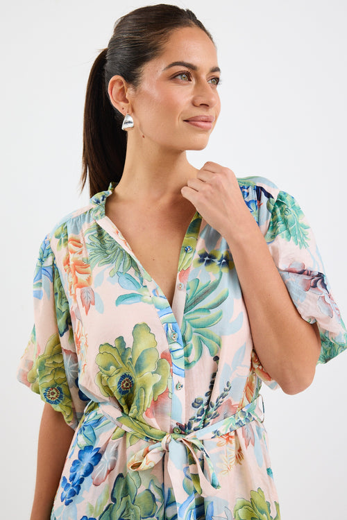 Woman wearing a colourful floral mini dress with a waist tie, short sleeves, and a tiered skirt.







