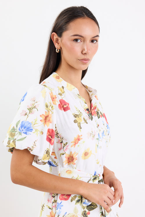 Woman wearing a cream floral mini dress with a tie belt, button front, short puff sleeves, and a drop waist design.