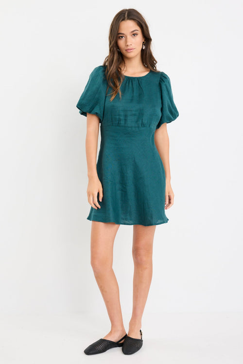 Woman wearing a forest green mini dress with puff sleeves, bias-cut shape, and fitted waist, styled simply for an elegant look.