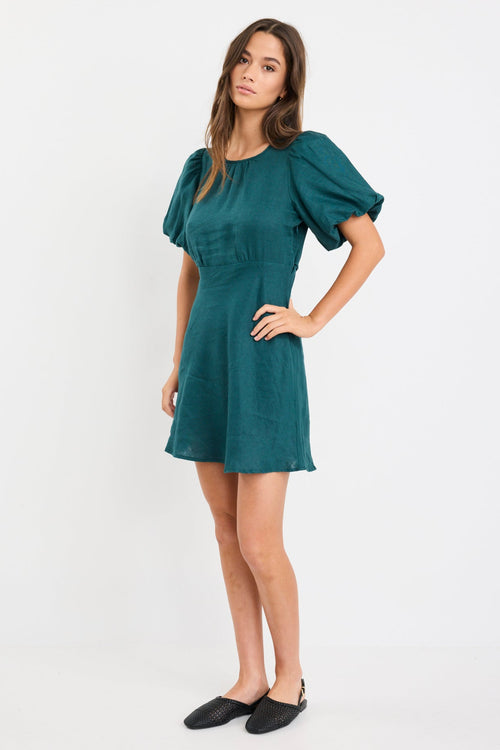 Woman wearing a forest green mini dress with puff sleeves, bias-cut shape, and fitted waist, styled simply for an elegant look.