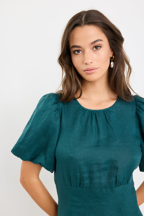 Woman wearing a forest green mini dress with puff sleeves, bias-cut shape, and fitted waist, styled simply for an elegant look.