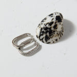 Two rings, one silver and one dalmatian jasper, on a textured white surface.