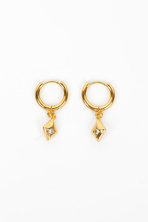 A pair of gold huggie hoop earrings with a small dangling geometric diamond-shaped charm, shown on a plain white background.