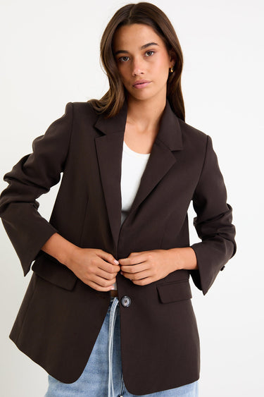 Woman wearing a brown blazer over a white shirt and blue jeans on a white background