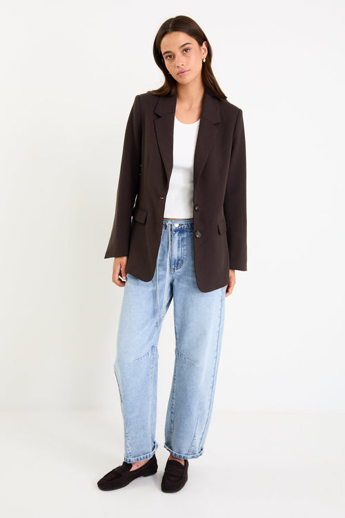 Model wearing a dark chocolate tailored blazer with a two-button front and vented sleeves.