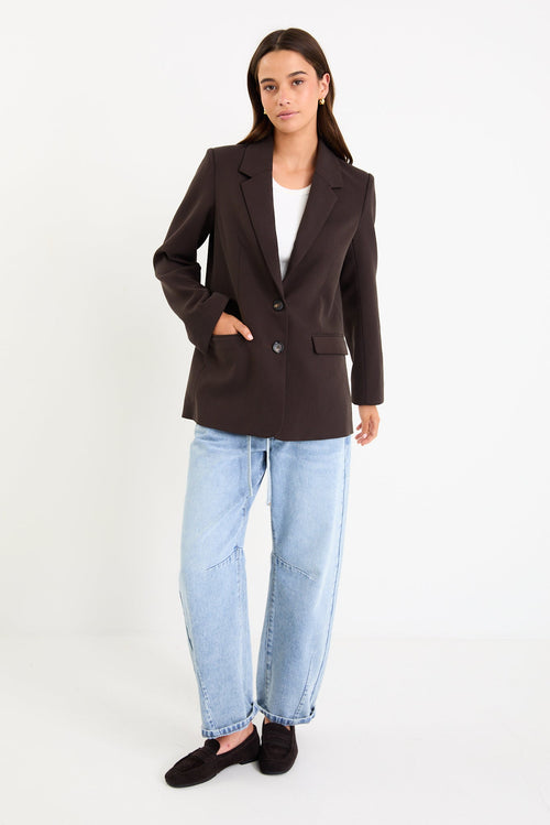 Model wearing a dark chocolate tailored blazer with a two-button front and vented sleeves.